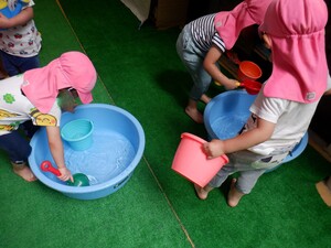 たらいに溜めた水で2歳児が水遊びをしています