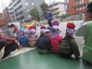 鬼のお面をかぶって保育士の話を聞く子どもの姿です。