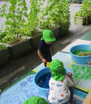 グリーンカーテンのあるベランダの前で水遊びをする子どもの写真